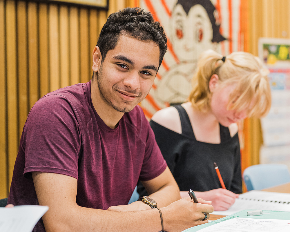 Teenage male student sitting at a desk studying and smiling