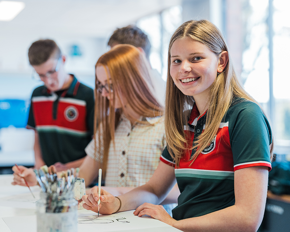 Teenage female student sitting at class desk smiling